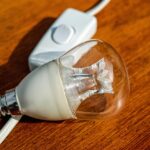 Lampadina fulminata in un lampadario con etichetta dei watt massimi del portalampada visibile.